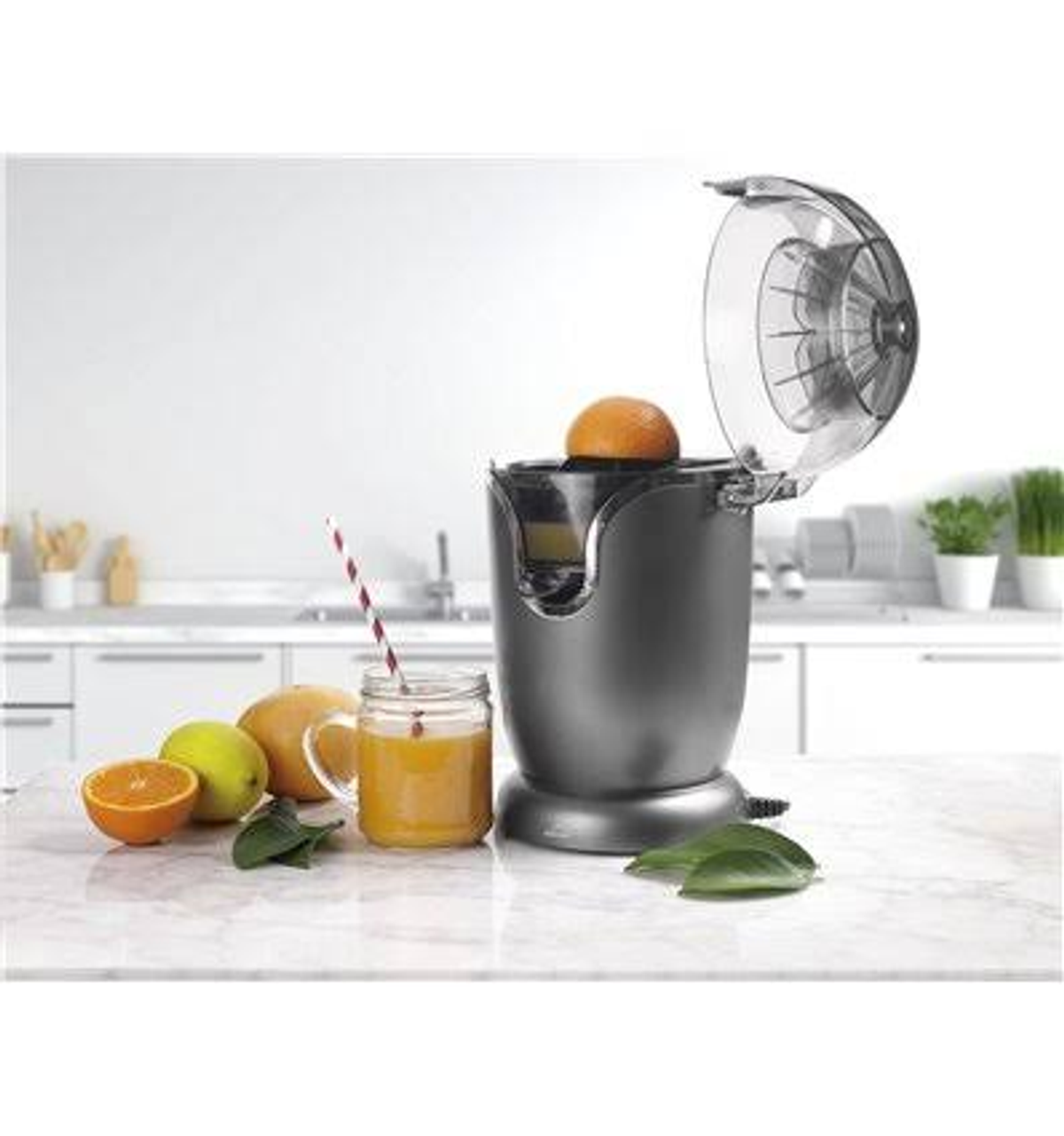 Spremiagrumi con arancia, succo in bicchiere e frutta accanto. Ambiente cucina.