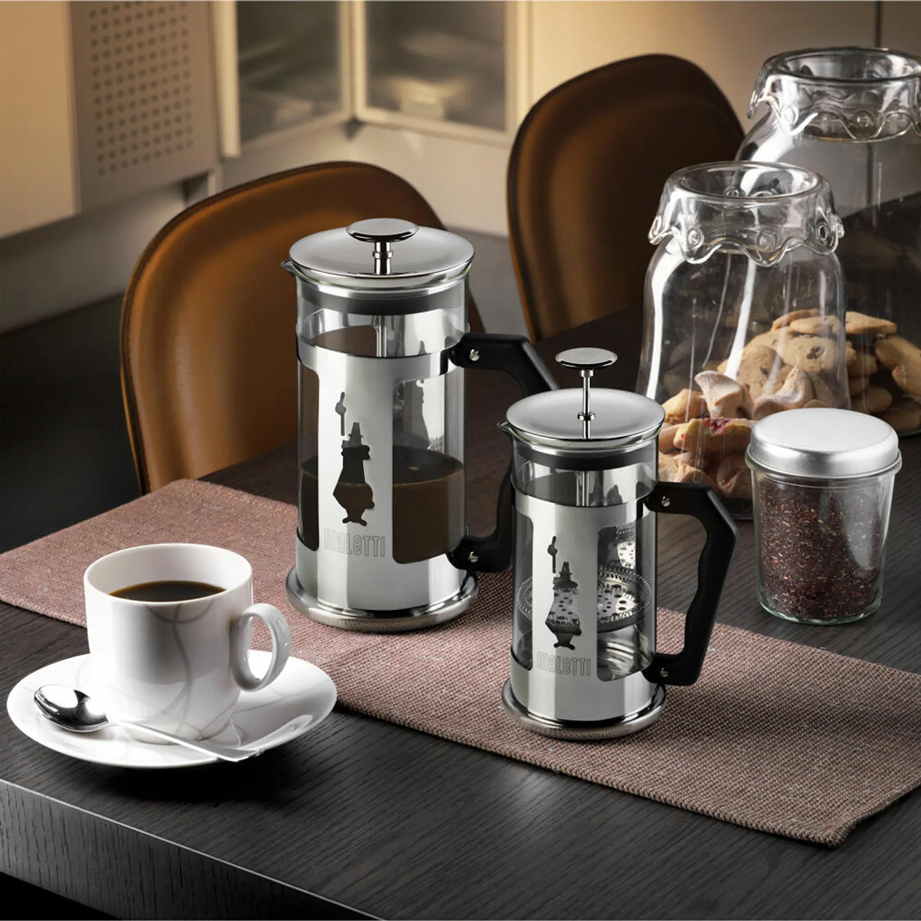 Ein Tisch mit zwei French Presses, einer Tasse Kaffee und einem Glas Keksen. Braun und Weiß dominieren.