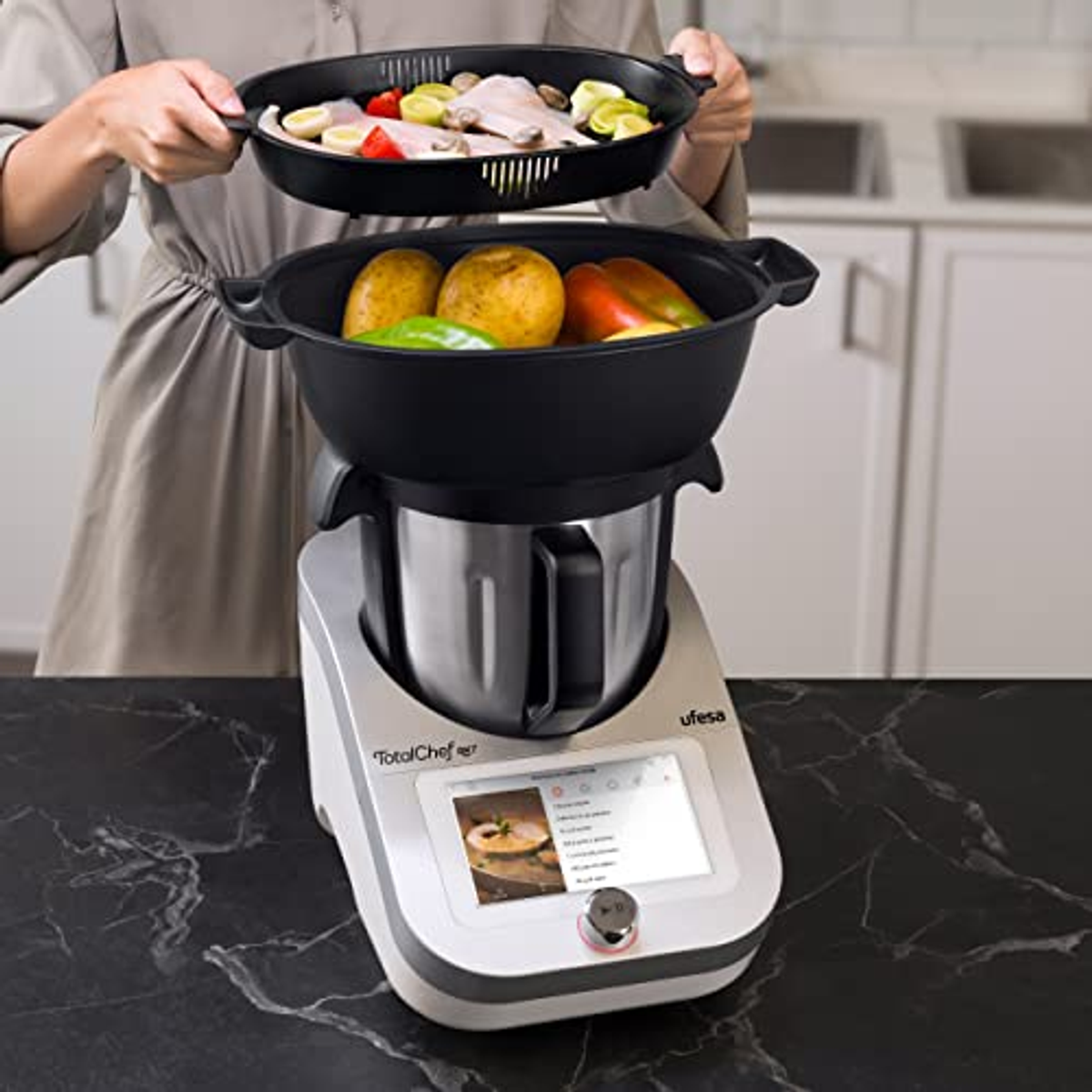 Person hält ein Tablett über eine TotalChef Küchenmaschine mit Bildschirm auf einem Tisch.