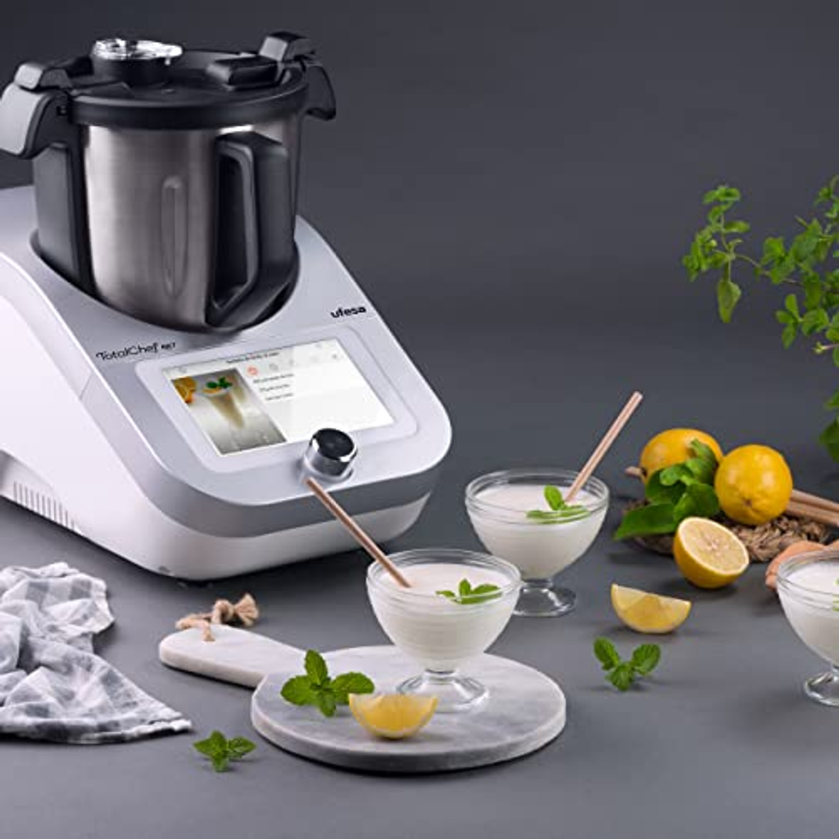 Küchenmaschine mit einer Schüssel Joghurt und Zitronen auf grauem Hintergrund.