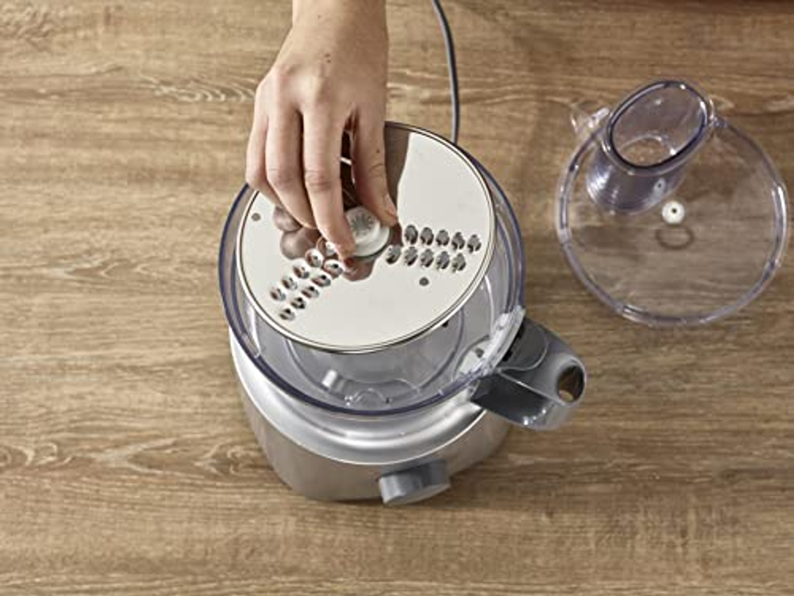 Mano di una persona che regola una lama su un robot da cucina. Sfondo con superficie in legno.