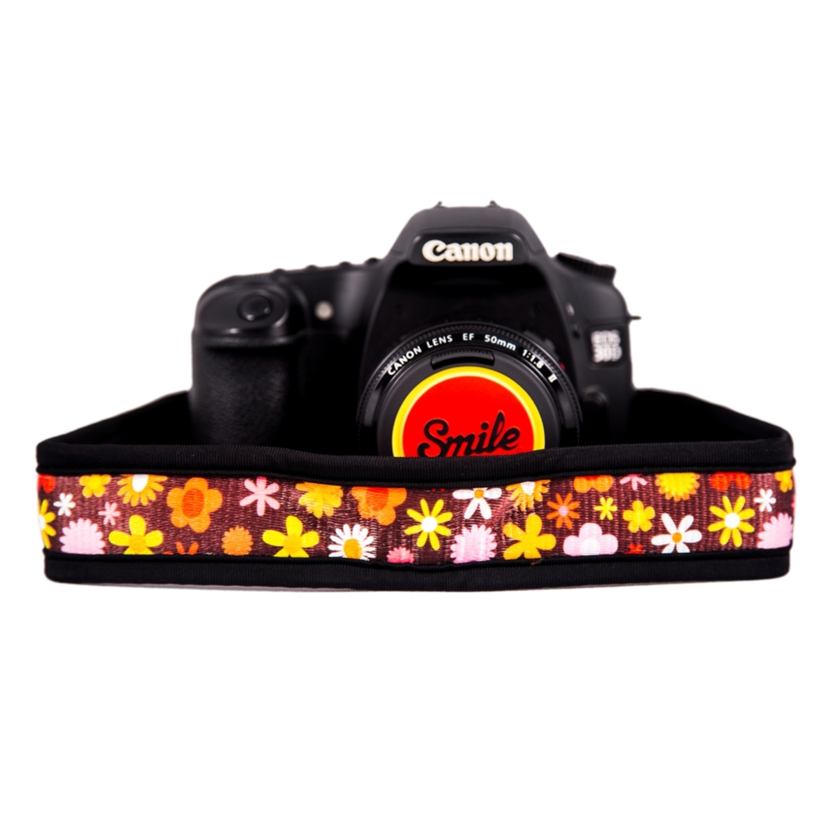 Una fotocamera Canon nera con obiettivo e cinturino colorato. Il cinturino ha un motivo floreale.