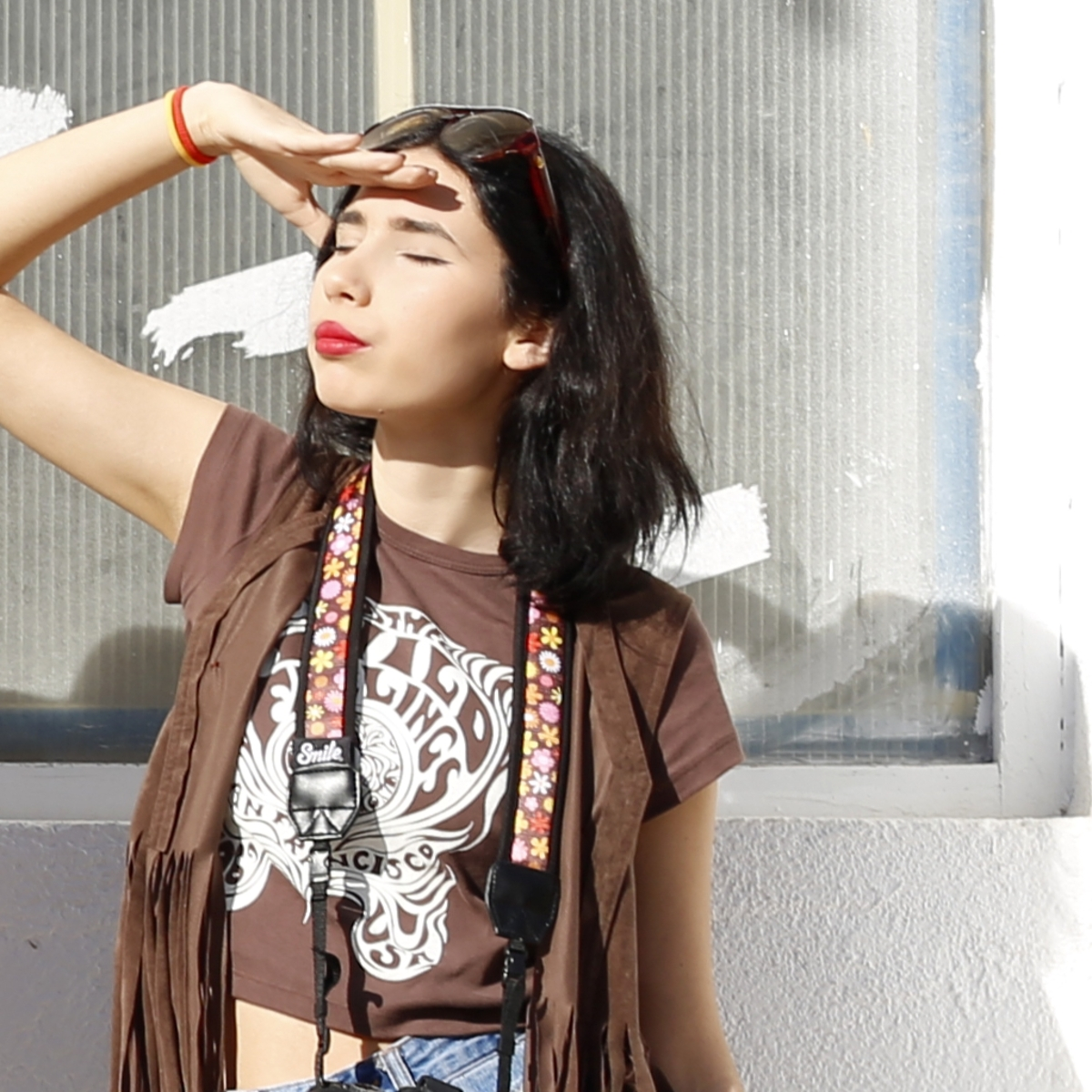 Una mujer se protege los ojos del sol, con gafas de sol y un top marrón. Está a la luz del sol.