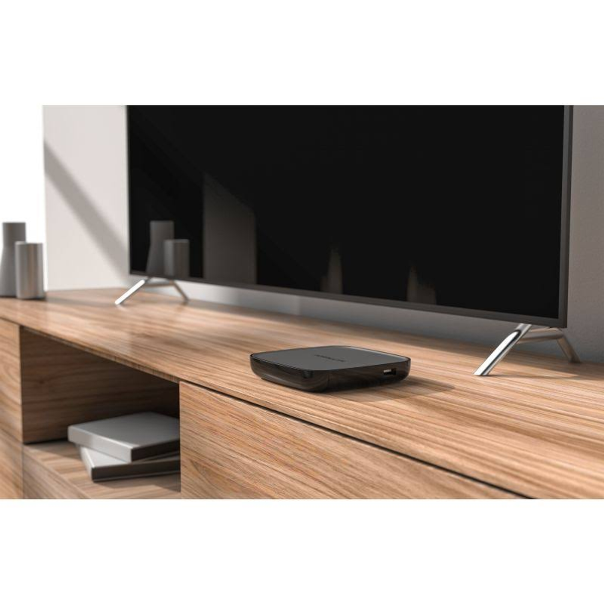 Schwarze TV-Box auf einem Holzschrank. Ein Flachbildfernseher ist im Hintergrund.