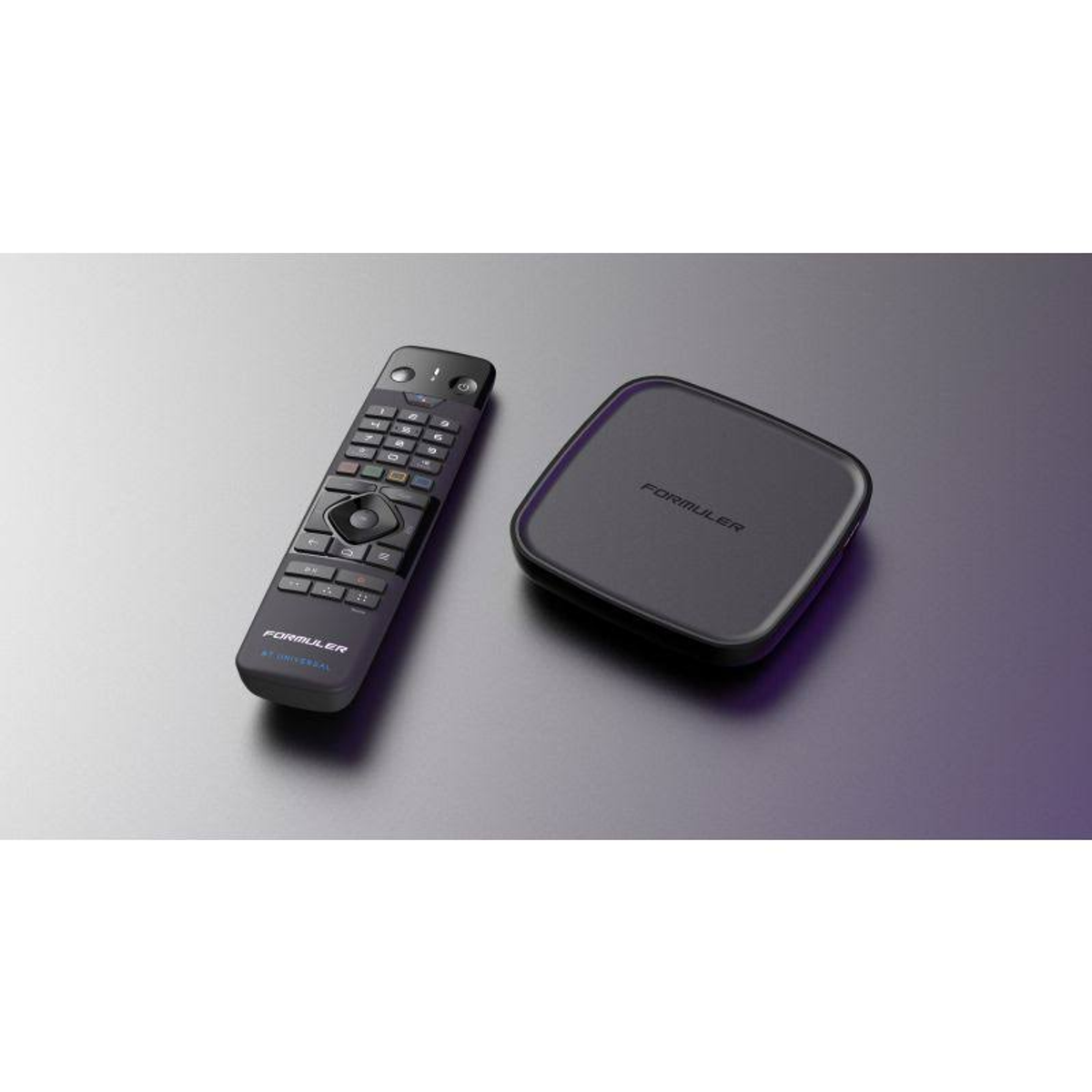 Schwarze Fernbedienung und Set-Top-Box auf grauer Oberfläche. Der Markenname ist auf beiden sichtbar.