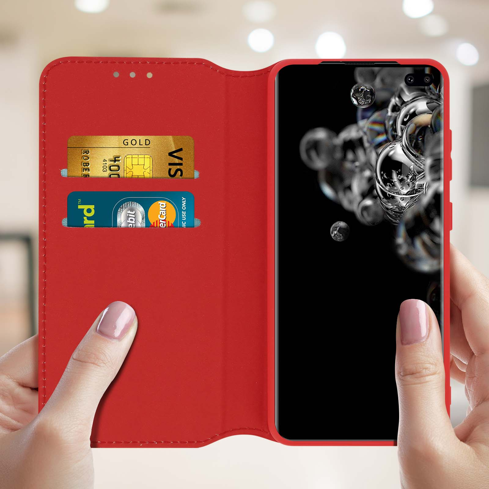 Una custodia rossa per telefono con una carta d'oro in uno slot e un telefono a destra, tenuta da due mani.