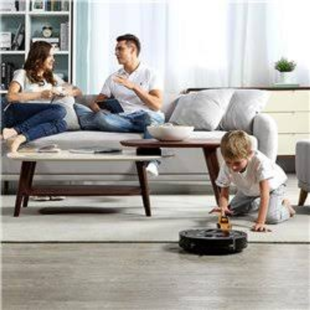 Familie auf Sofa, Kind spielt mit Roboterstaubsauger. Wohnzimmer.