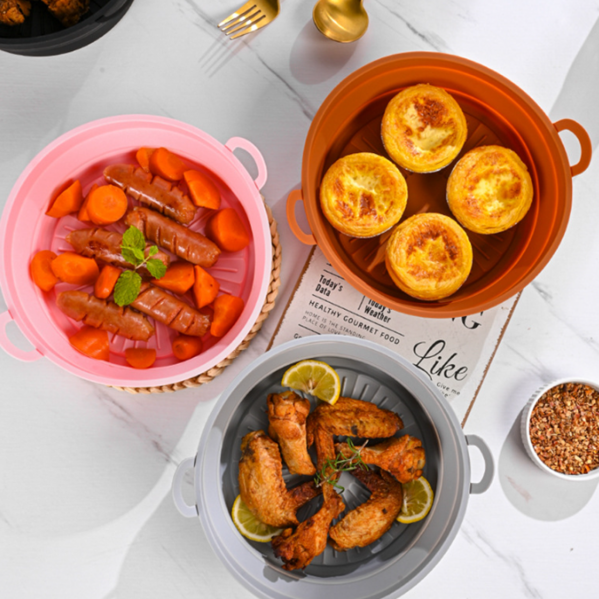 Drei Silikon-Airfryer-Körbe mit Essen: Würstchen und Karotten, Eiertörtchen und Hähnchenflügel.