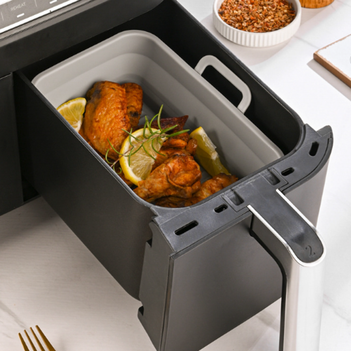 Luftfritteusen-Schublade offen, mit gebratenem Hähnchen und Zitronenscheiben darin. Griff und Bedienfeld sichtbar.