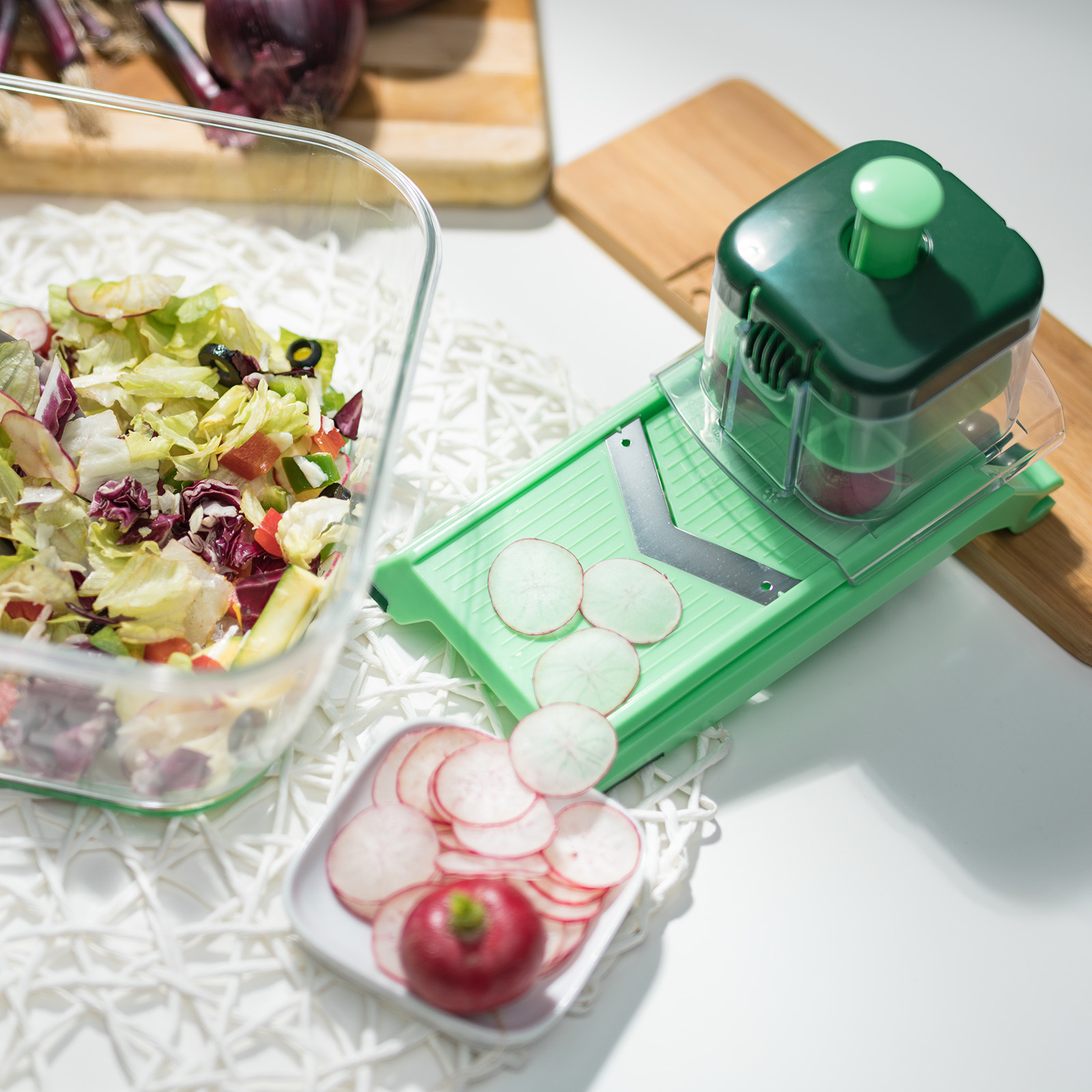 Grüner Gemüseschneider mit Radieschen und zubereitetem Salat auf weißer Oberfläche.