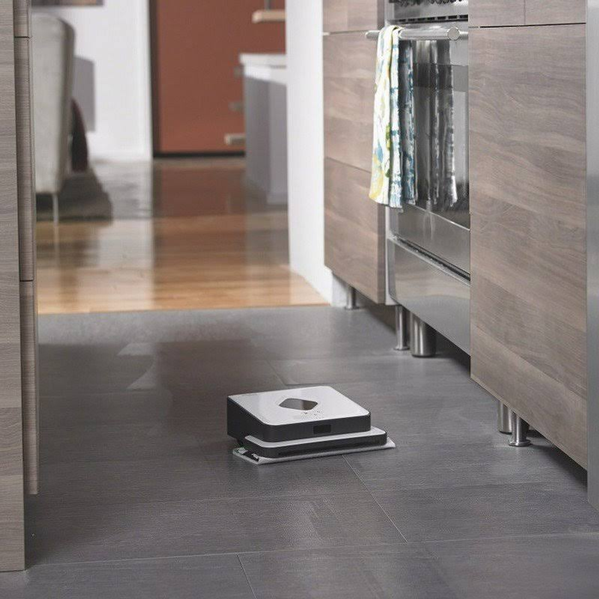Ein Roboter-Staubsauger auf einem grauen Boden in einem Küchenbereich.