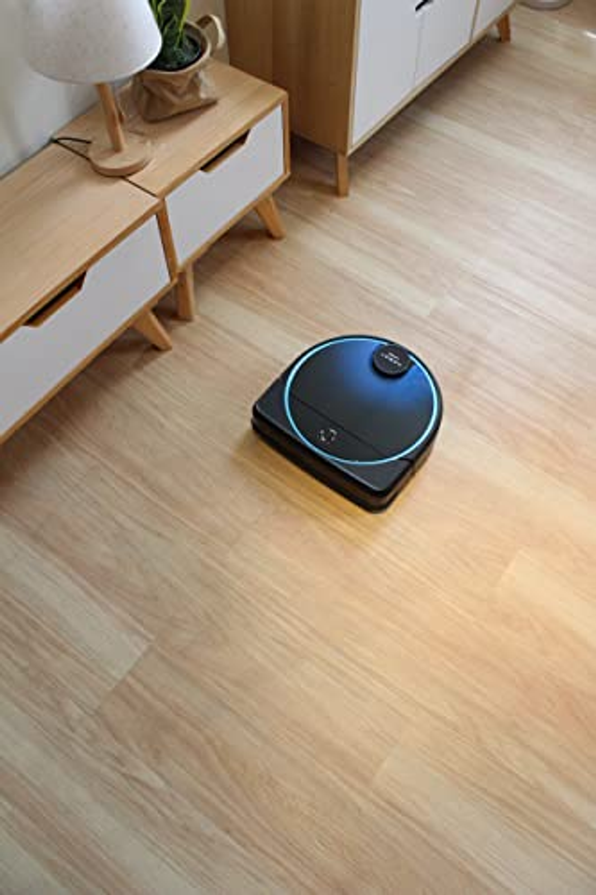 Aspiradora robot negra en suelo de madera. Hay un armario al fondo.