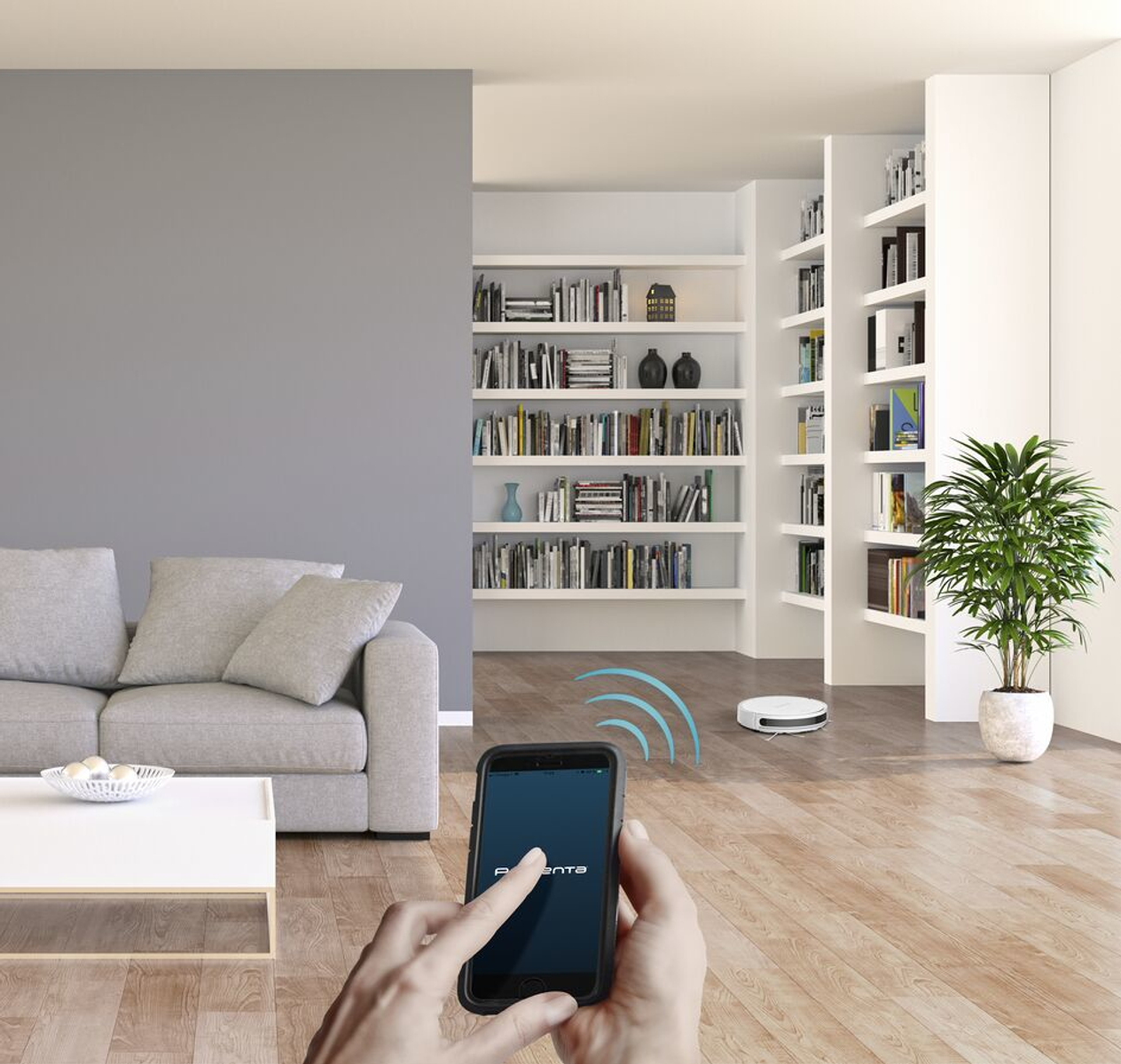 Osoba używająca telefonu do sterowania robotem sprzątającym w nowoczesnym salonie z regałem na książki.