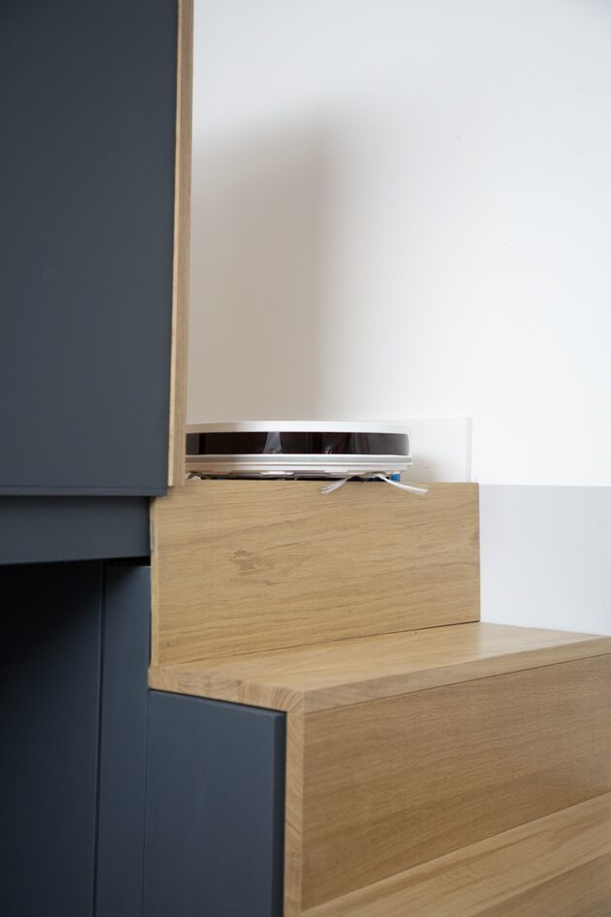 Robot sprzątający na drewnianym stopniu, częściowo ukryty. Szare i drewniane odcienie.