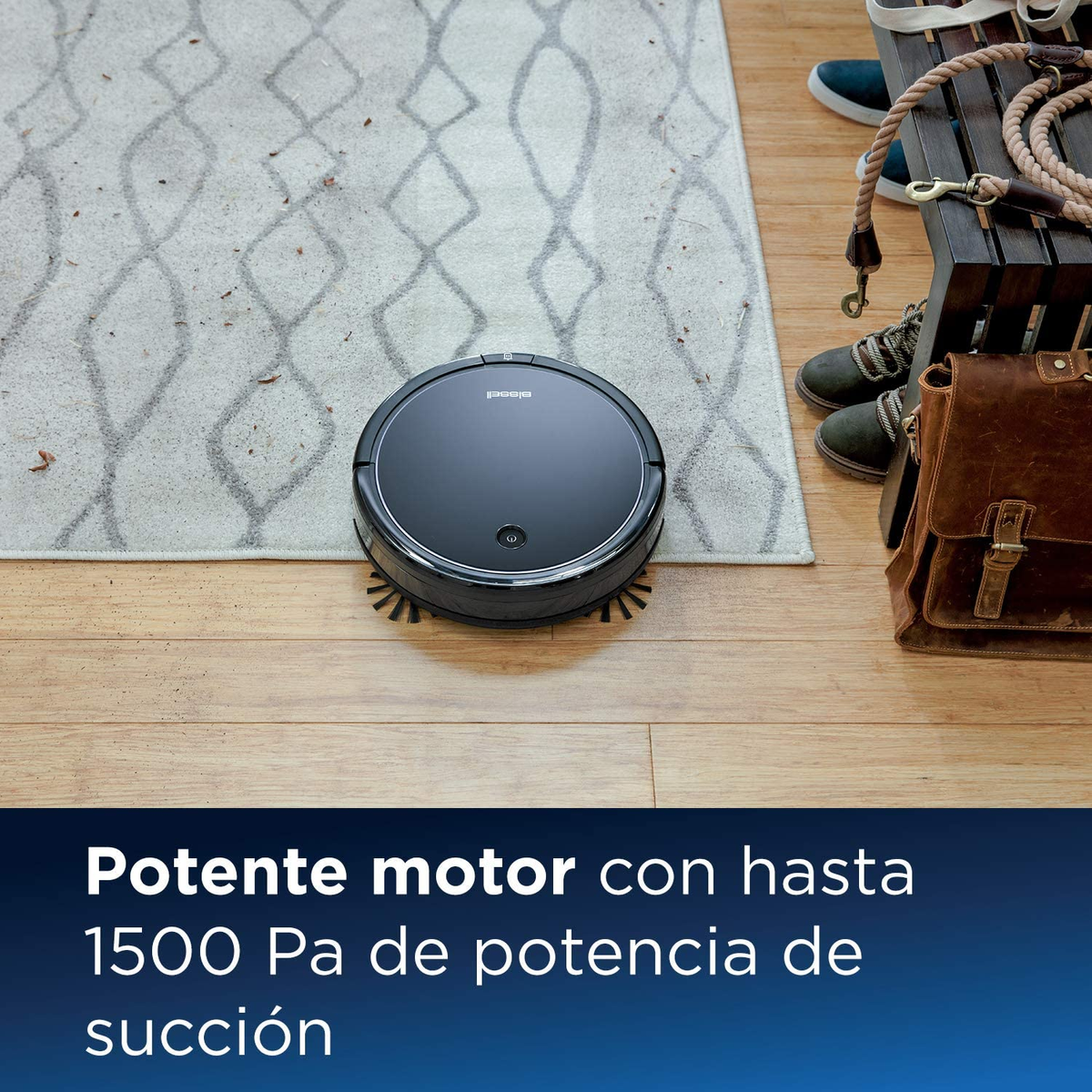 Una aspiradora robot negra en un piso de madera junto a una alfombra y una bolsa de cuero.