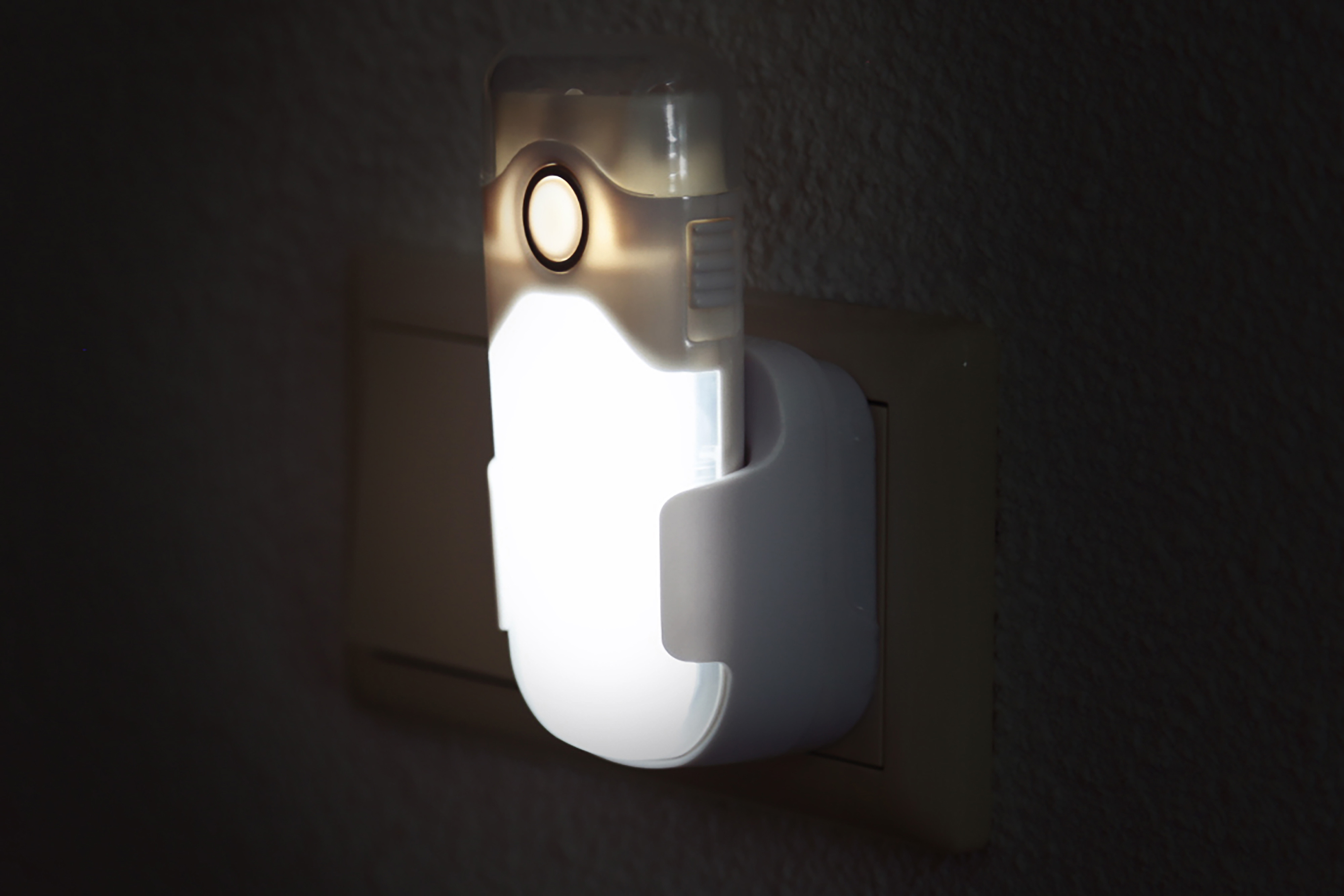 A white night light plugged into a wall outlet, glowing with bright light.