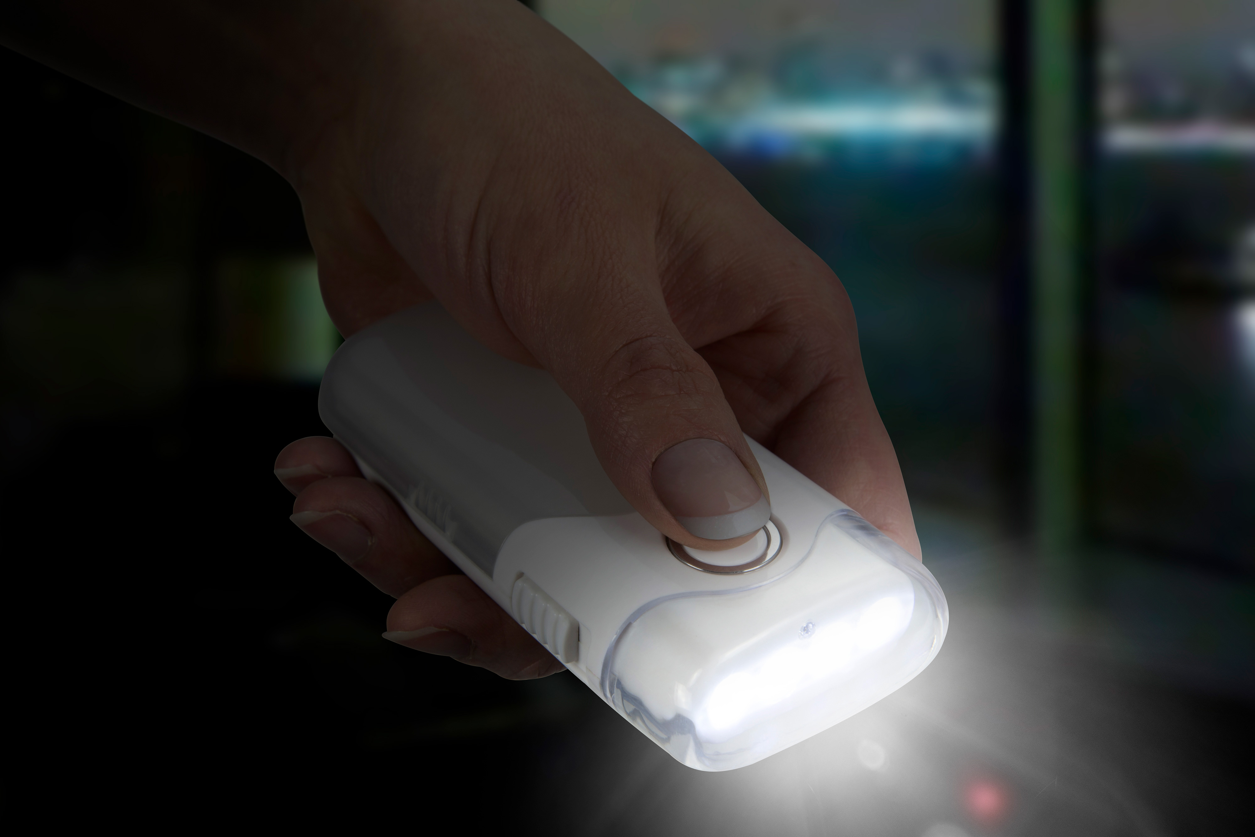 A hand holding a white flashlight with a bright light beam. The background is dark and out of focus.