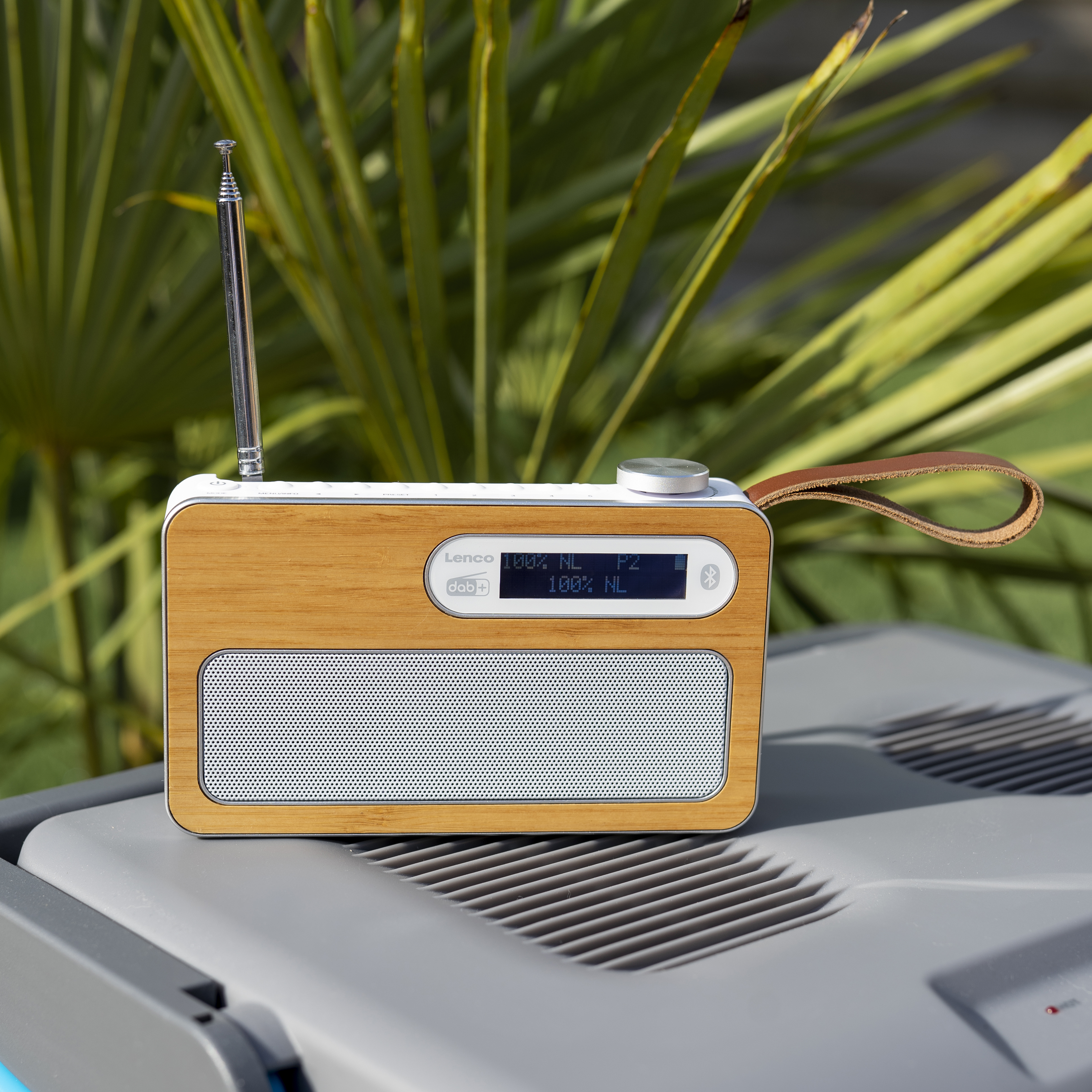 Ein Holzradio mit Antenne, Ledergriff und Digitalanzeige, platziert auf einer grauen Oberfläche.