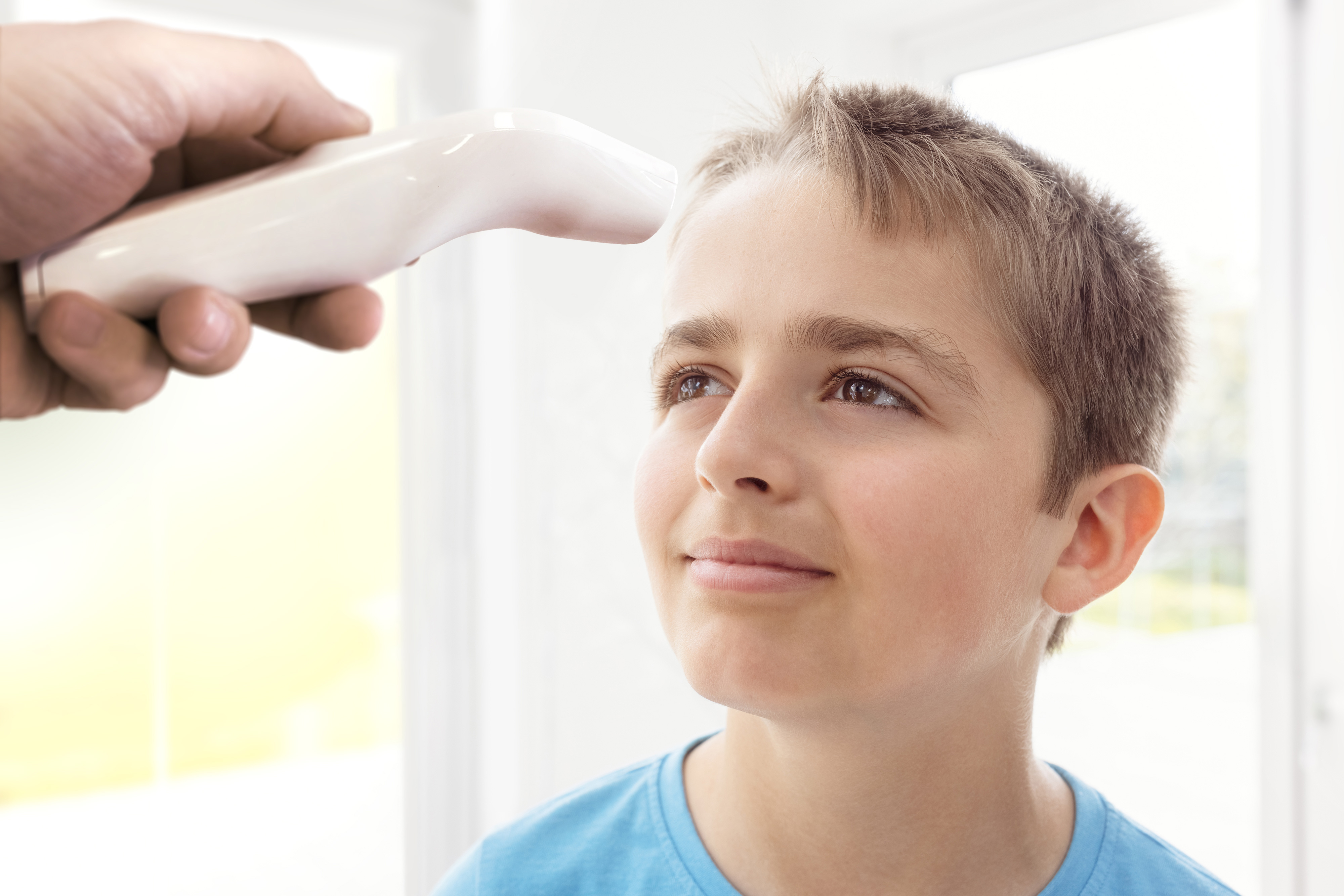 Eine Hand hält ein weißes Thermometer in der Nähe der Stirn eines Jungen und misst seine Temperatur.