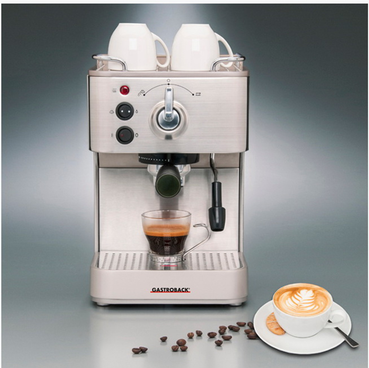 Espressomaschine mit Kaffee, Bohnen und zwei Tassen oben. Silberfarbenes Design.