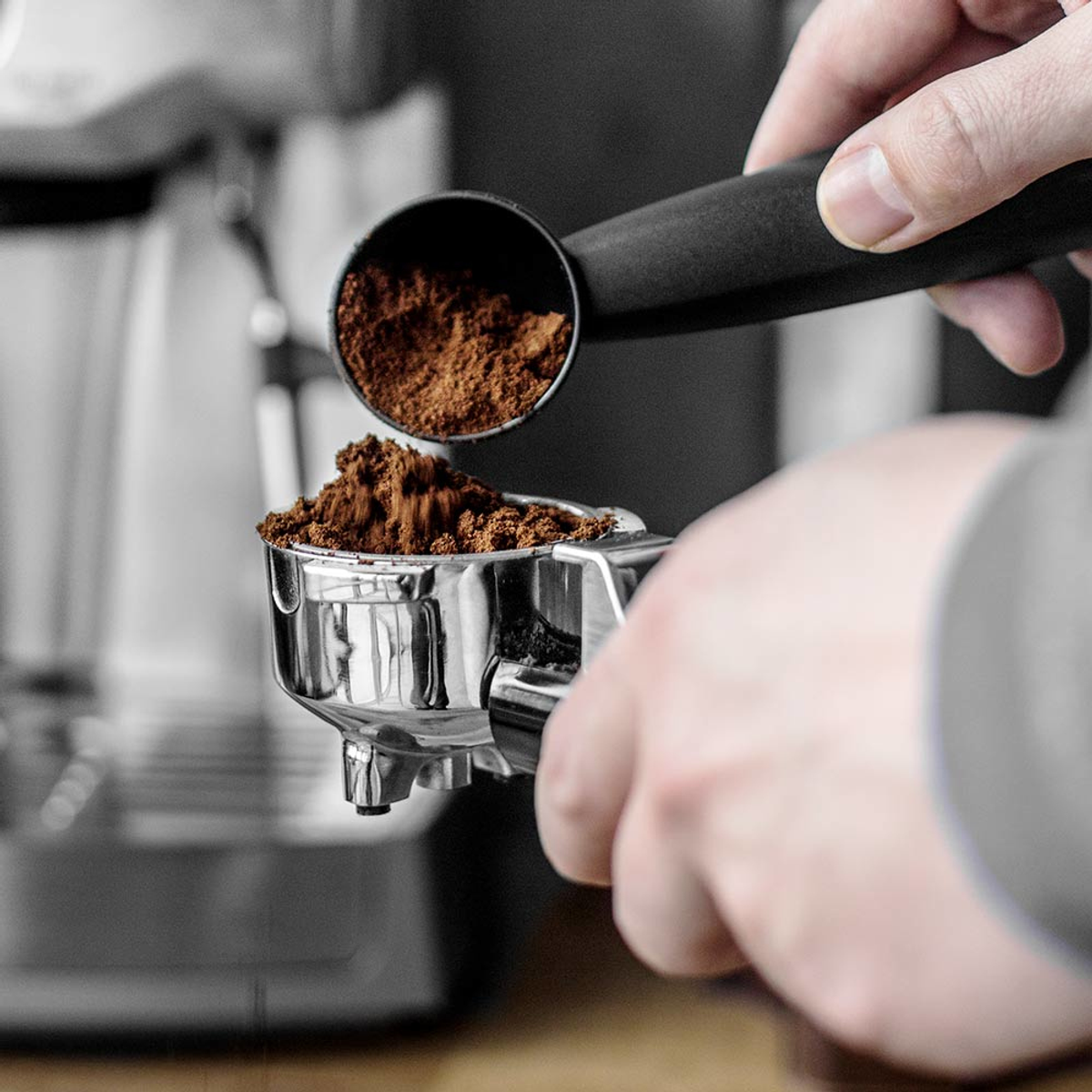 Ręce osoby napełniającej kolbę zmieloną kawą za pomocą miarki.