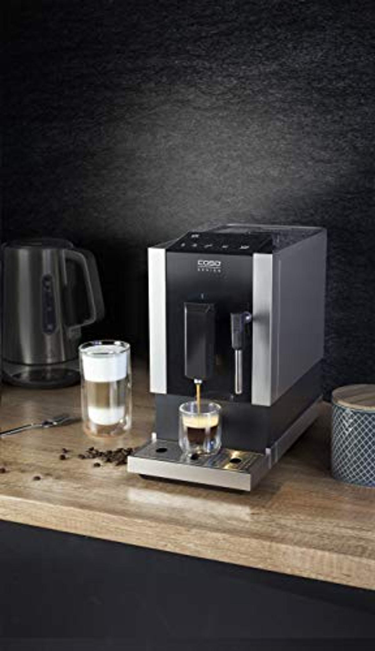 Macchina per caffè espresso con design nero e argento, versa il caffè in un bicchiere trasparente.