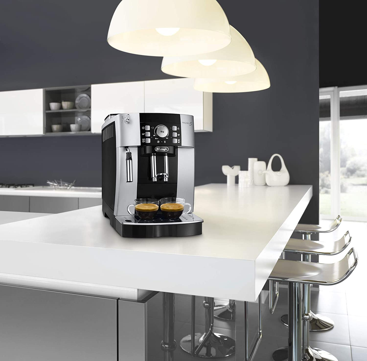 Máquina de espresso en una encimera blanca, con dos tazas de café y tres lámparas colgantes.