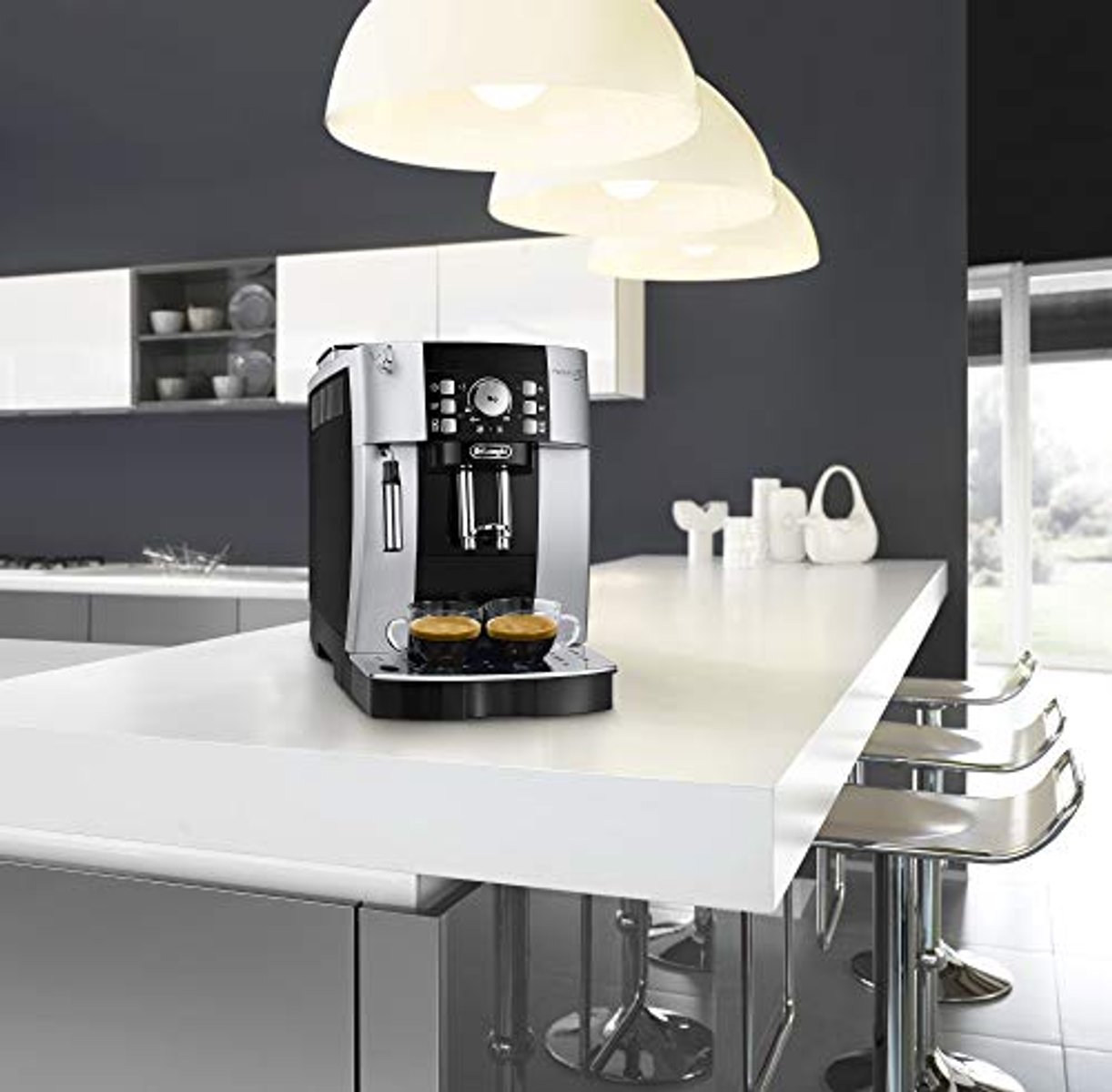Máquina de espresso en mostrador. Dos tazas de café y luces colgantes visibles.