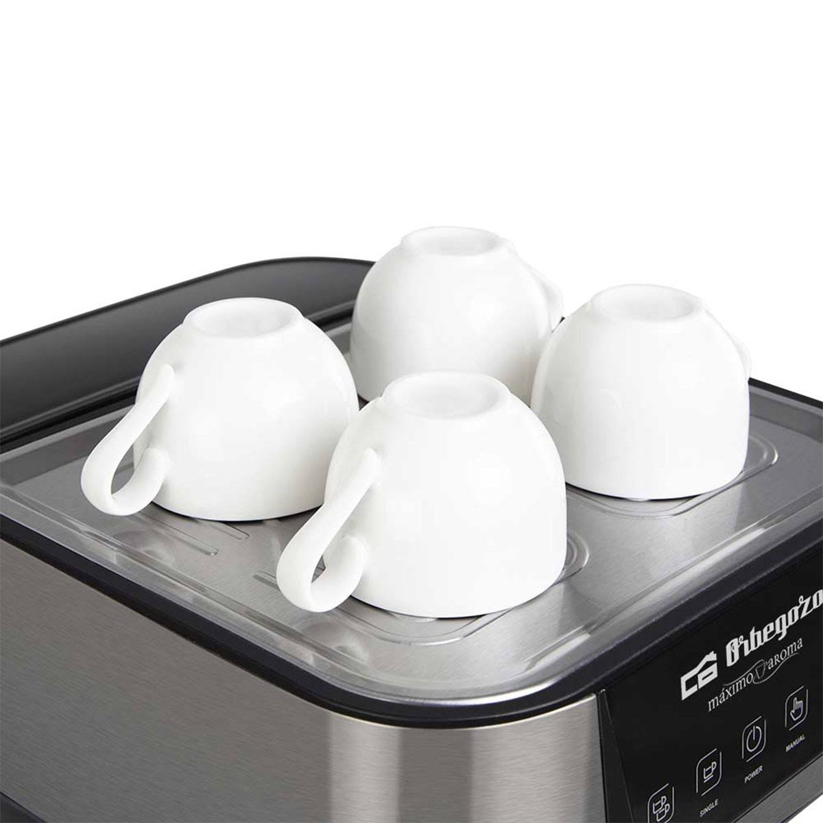 Cztery białe filiżanki do kawy na podgrzewaczu ze stali nierdzewnej. W tle widoczny ekspres do kawy.