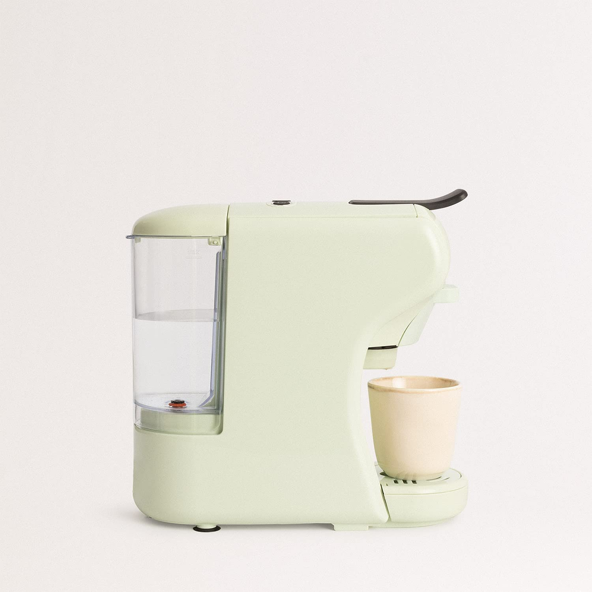 Una cafetera verde claro con depósito de agua y taza beige.