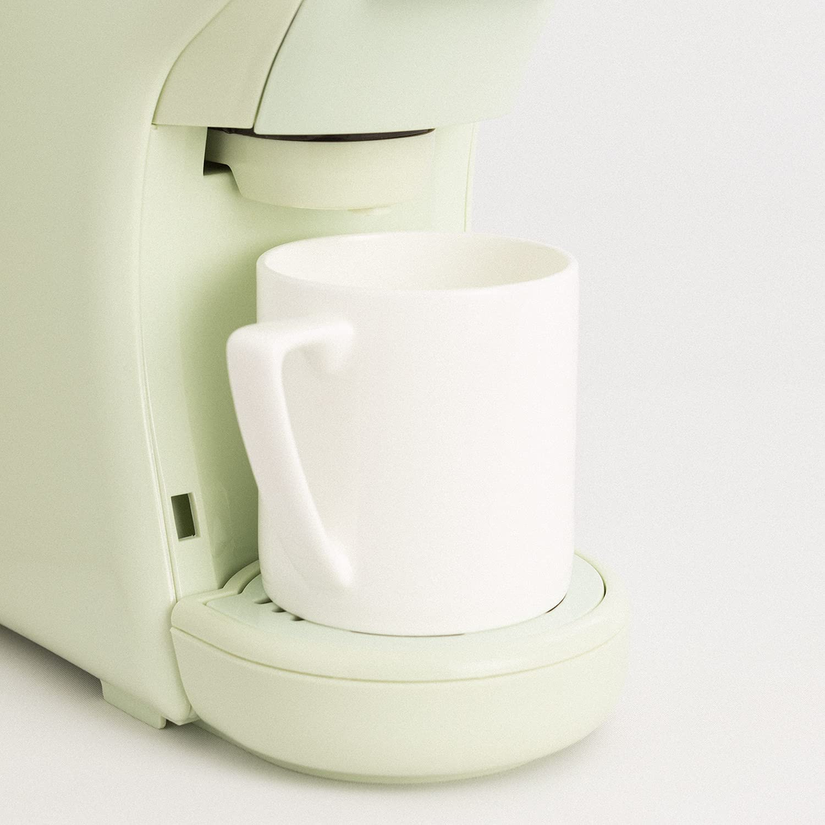 Cafetera con una taza blanca. Máquina verde claro con fondo blanco.