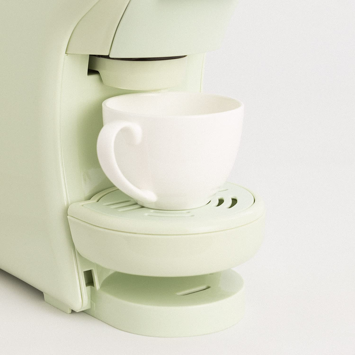 Una cafetera verde con una taza blanca en la bandeja de goteo. La taza está vacía.
