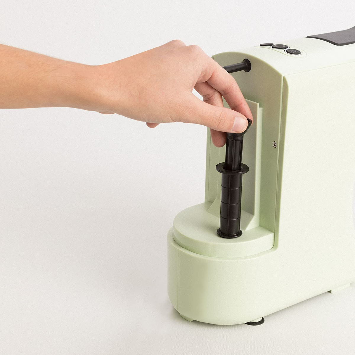 La mano de una persona insertando una pieza en un electrodoméstico de cocina verde claro.