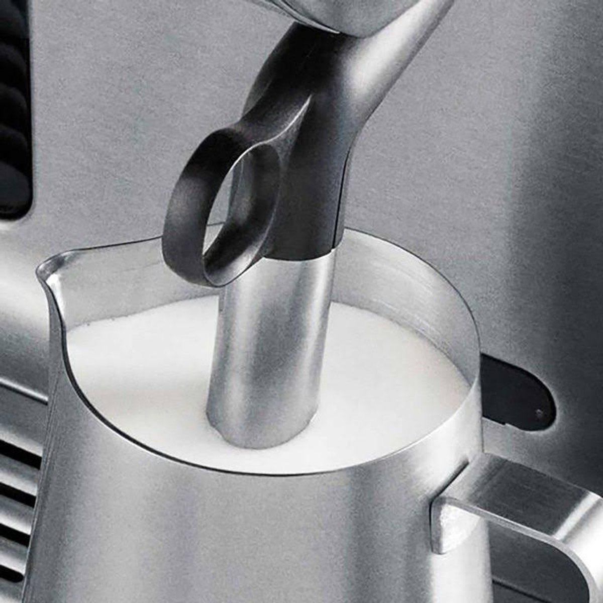 Ein Milchschaumkännchen aus Metall mit Milch und einem Aufschäumer.