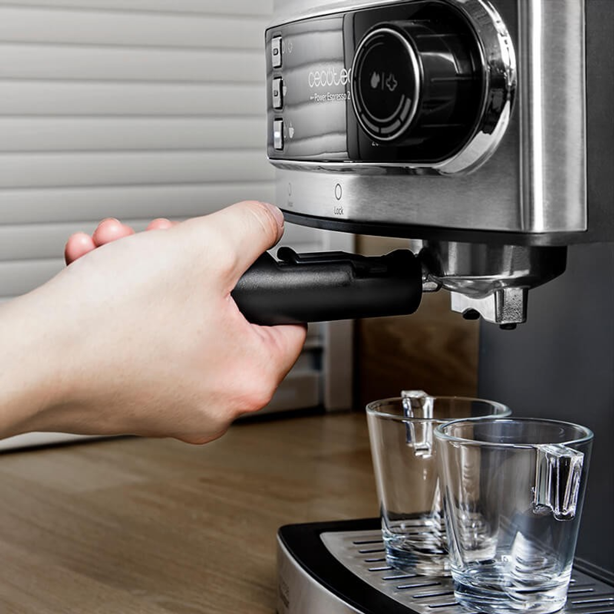 Hand hält einen schwarzen Siebträger an eine Kaffeemaschine, zwei leere Gläser.