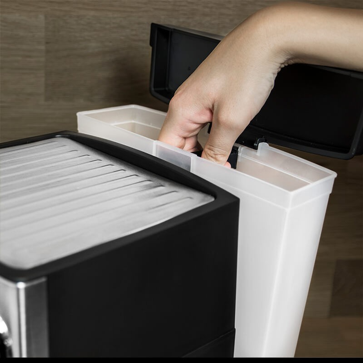 Die Hand einer Person, die einen weißen Behälter in eine schwarze Kaffeemaschine einsetzt, mit einer Kaffeetasse in der Nähe.