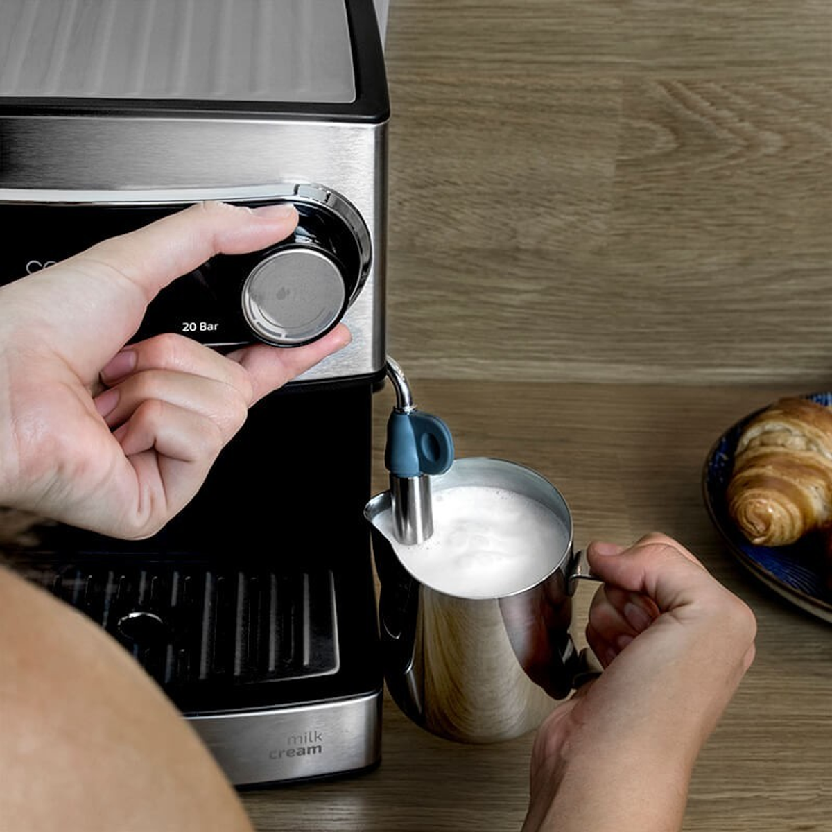 Eine Person, die Milchschaum mit einem Edelstahlkrug und einer Kaffeemaschine zubereitet.