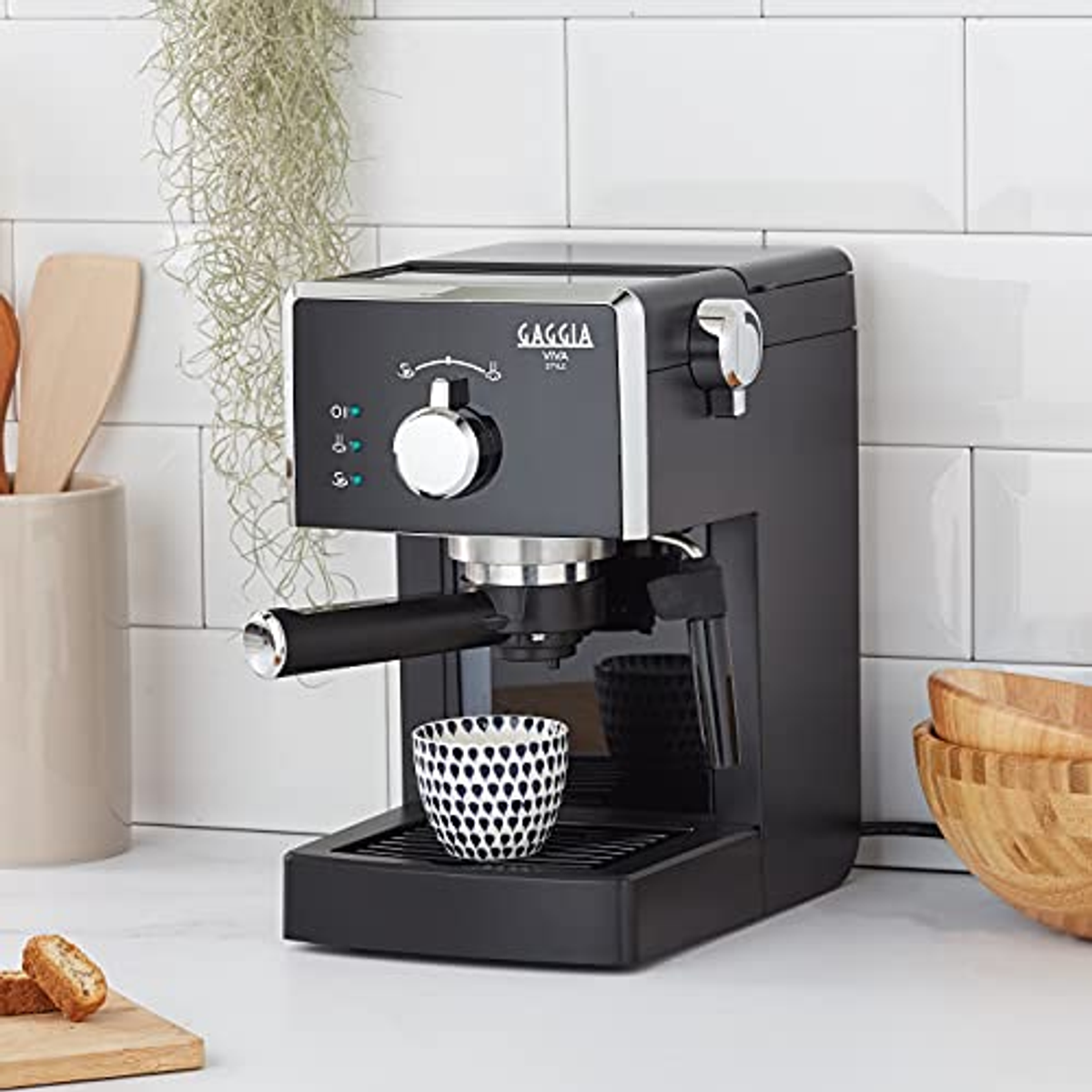 Máquina de espresso Gaggia Viva Style, negra, con una taza y cuencos de madera al fondo.