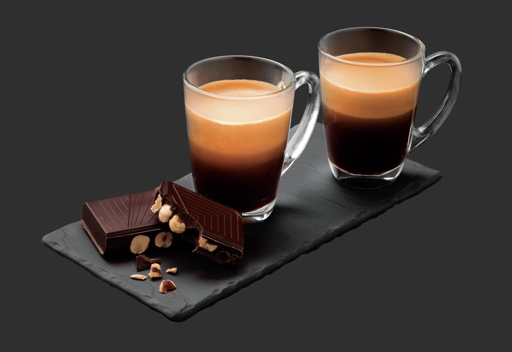 Dwie filiżanki kawy z czekoladą i batonami z orzechami laskowymi na czarnej powierzchni.