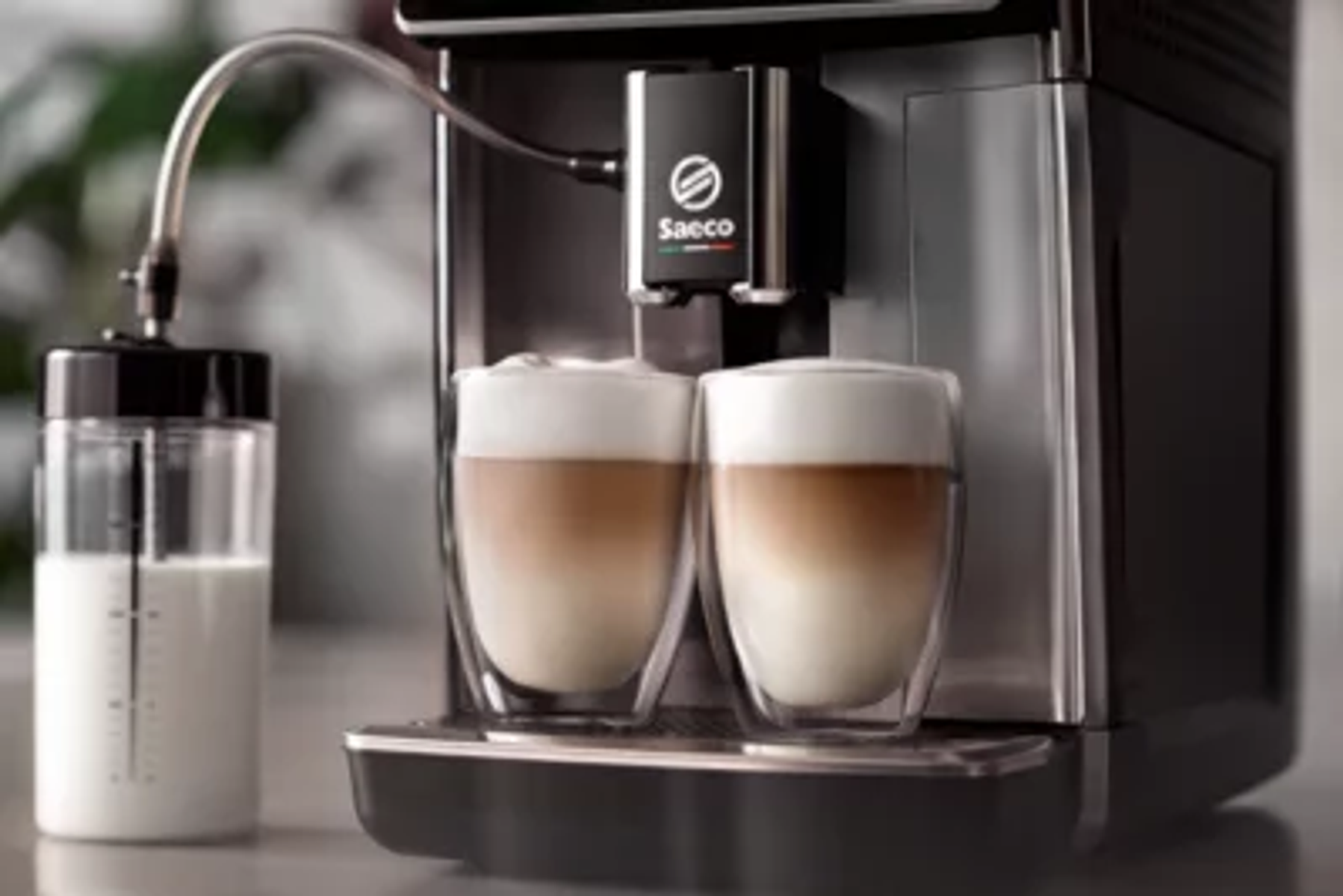 Eine Kaffeemaschine, die zwei Lattes zubereitet. Ein Milchbehälter befindet sich links. Die Maschine hat das Saeco-Logo.