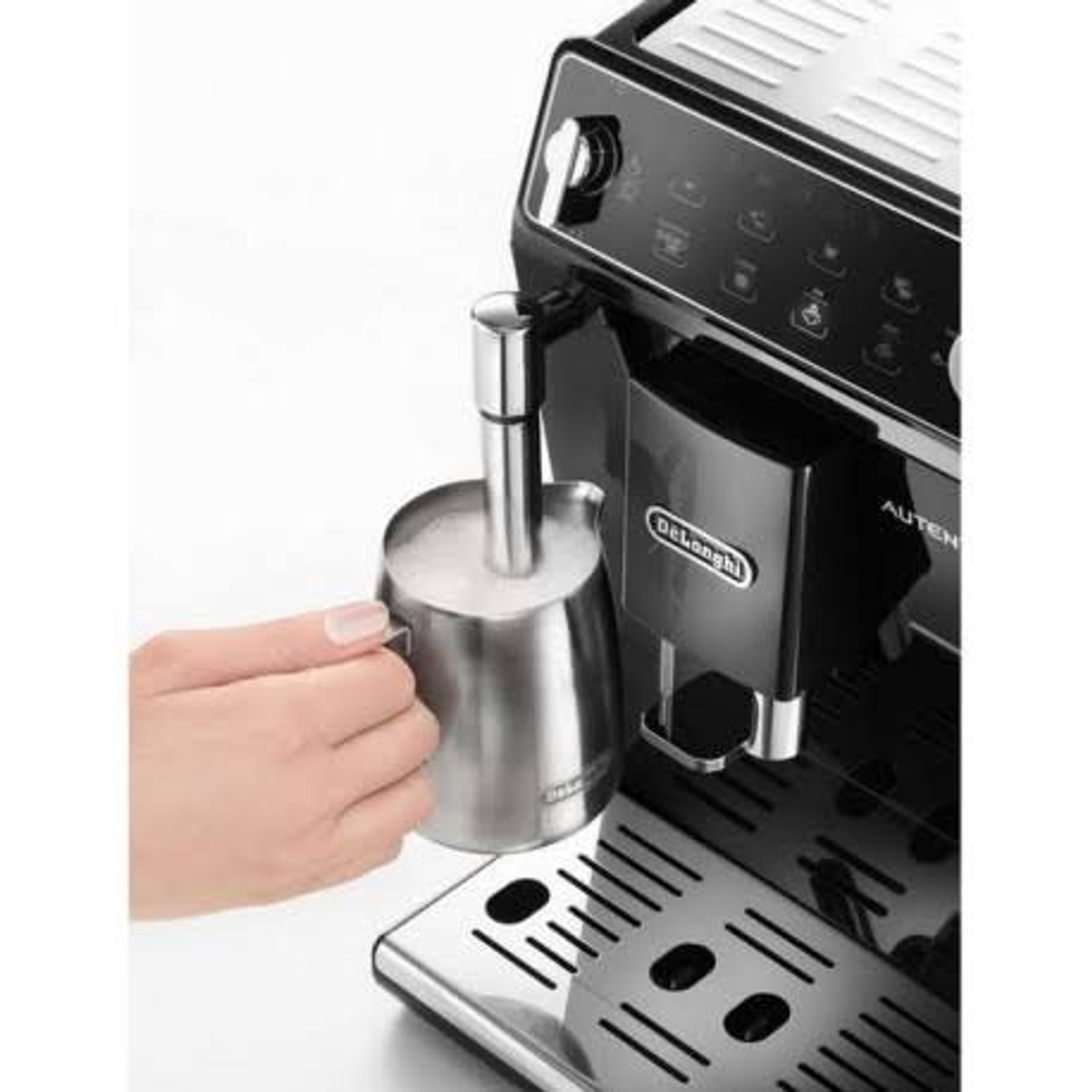 Una mano sostiene una jarra de acero cerca de una máquina de café espumando leche.
