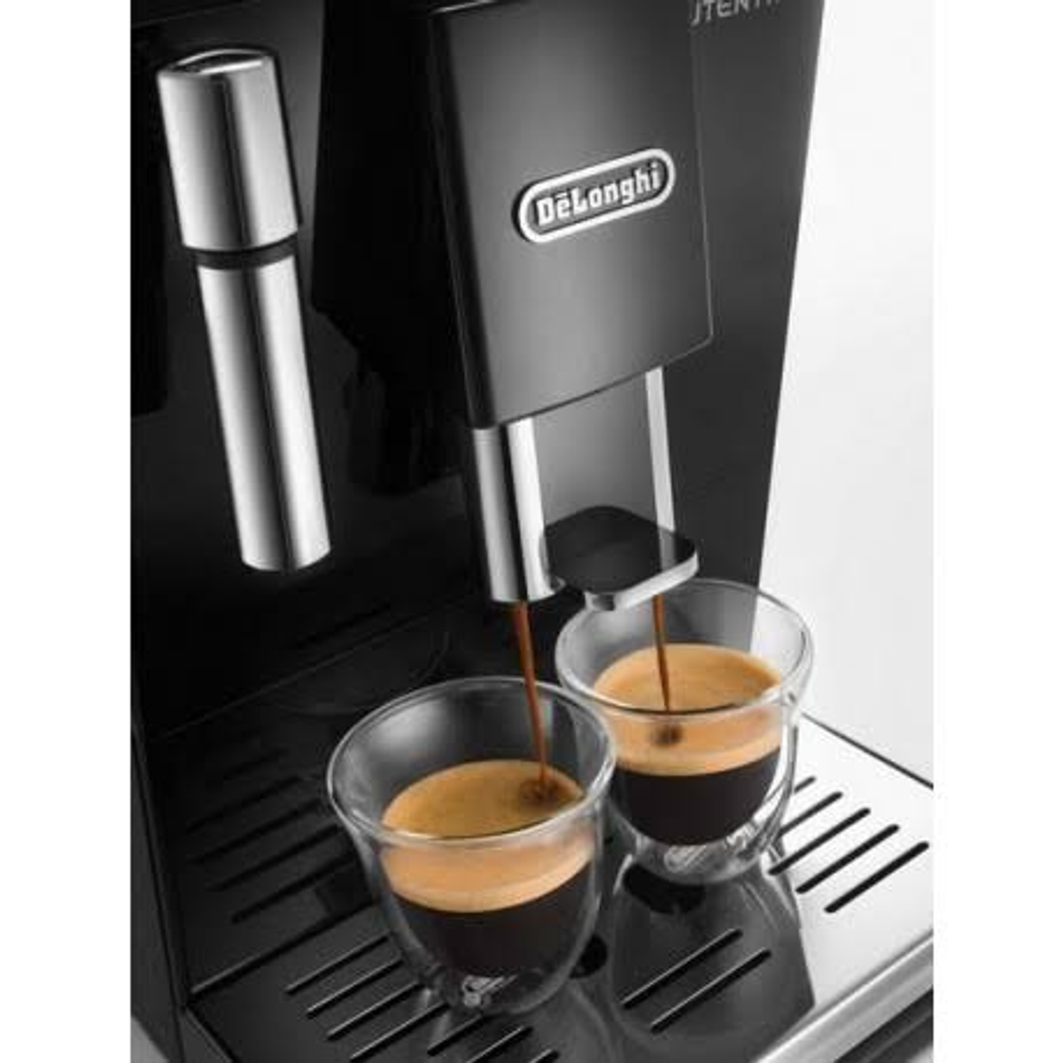 Cafetera dispensando espresso en dos tazas de vidrio transparente. Vapor visible.