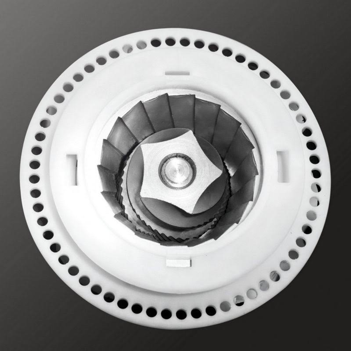 Widok z góry na białą szlifierkę z czarnym środkiem i wieloma otworami na krawędzi.