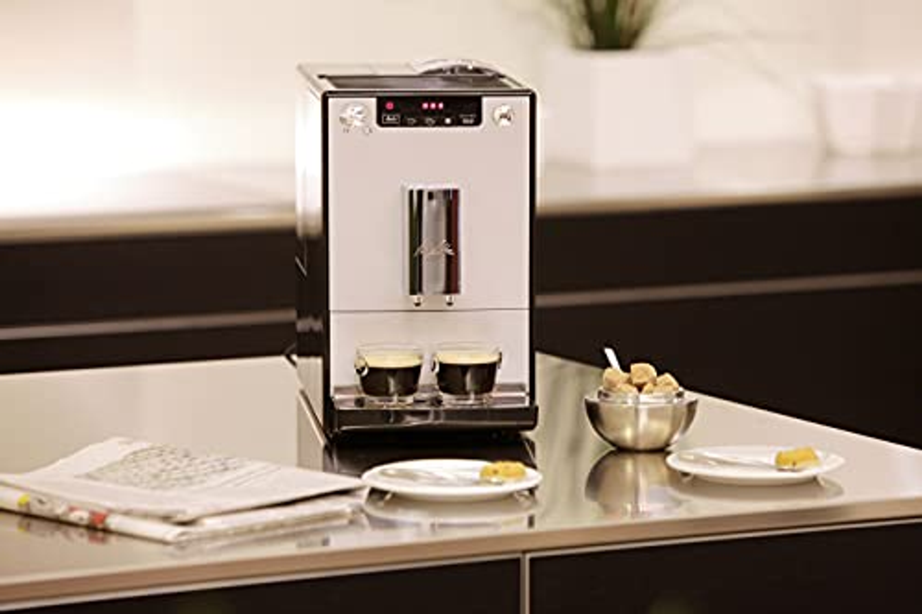 Una cafetera con dos espressos, cubos de azúcar y pasteles en una mesa.