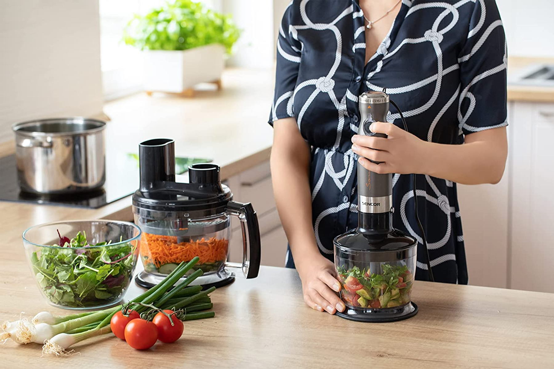 Donna usa un frullatore a immersione in cucina con ingredienti per l'insalata.