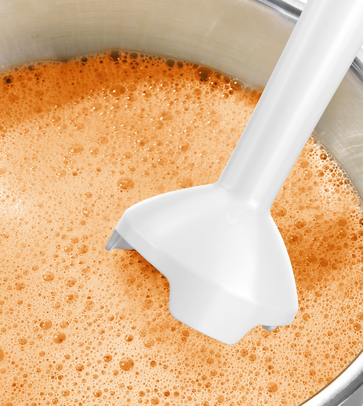 Ein weißes Stabmixermesser in einer metallischen Schüssel mit orangefarbener Flüssigkeit. Die Flüssigkeit blubbert.