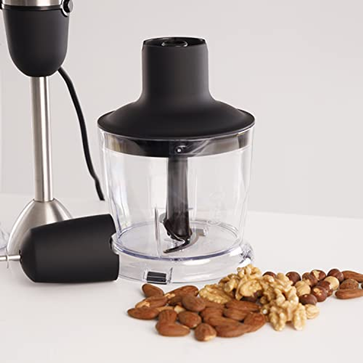 Batidora de mano con parte superior negra, recipiente transparente y nueces.
