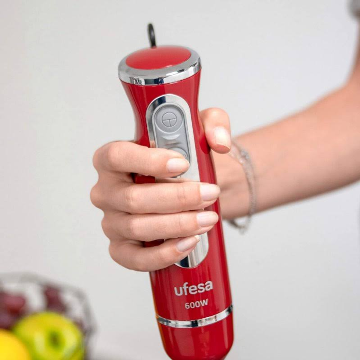 Mano che tiene un frullatore a immersione rosso con un pulsante argentato. Il marchio è Ufesa.