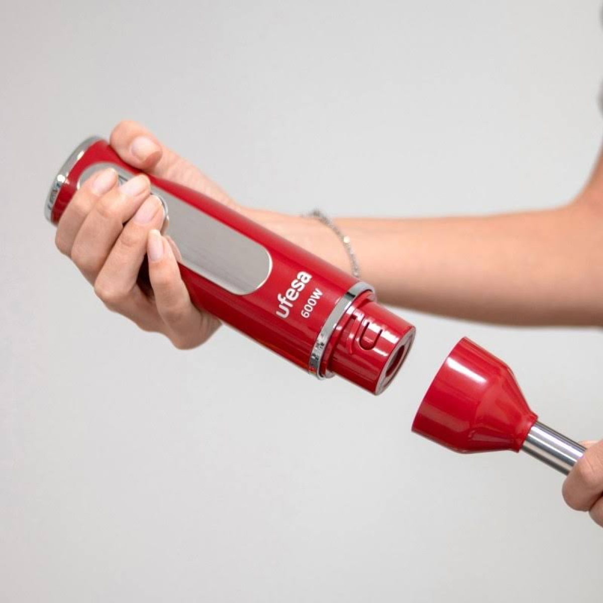Un frullatore a immersione rosso con l'accessorio per frullare staccato, tenuto da una mano.