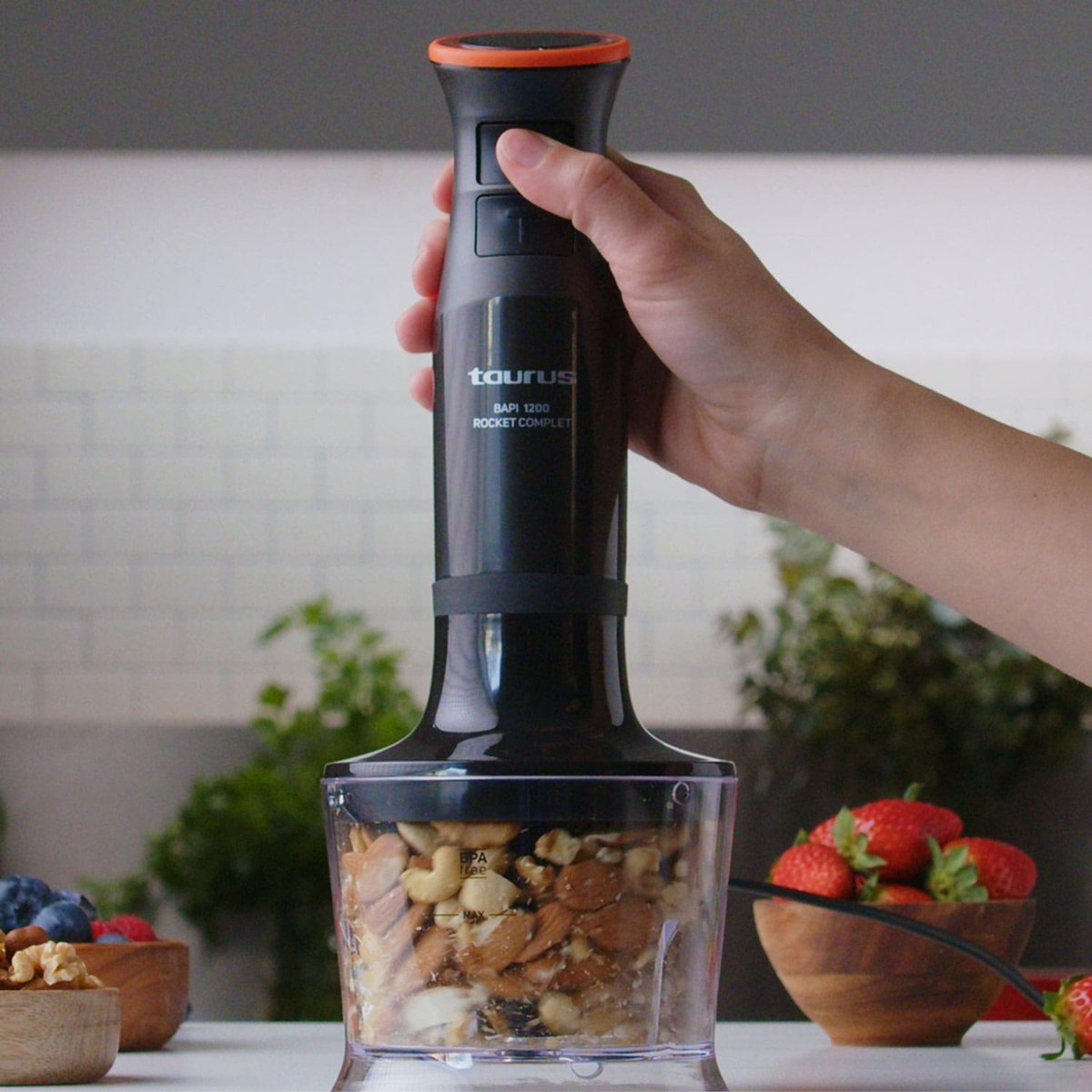 Czarny i srebrny blender Taurus w użyciu. Kubek zawiera orzechy. Ręka trzyma.